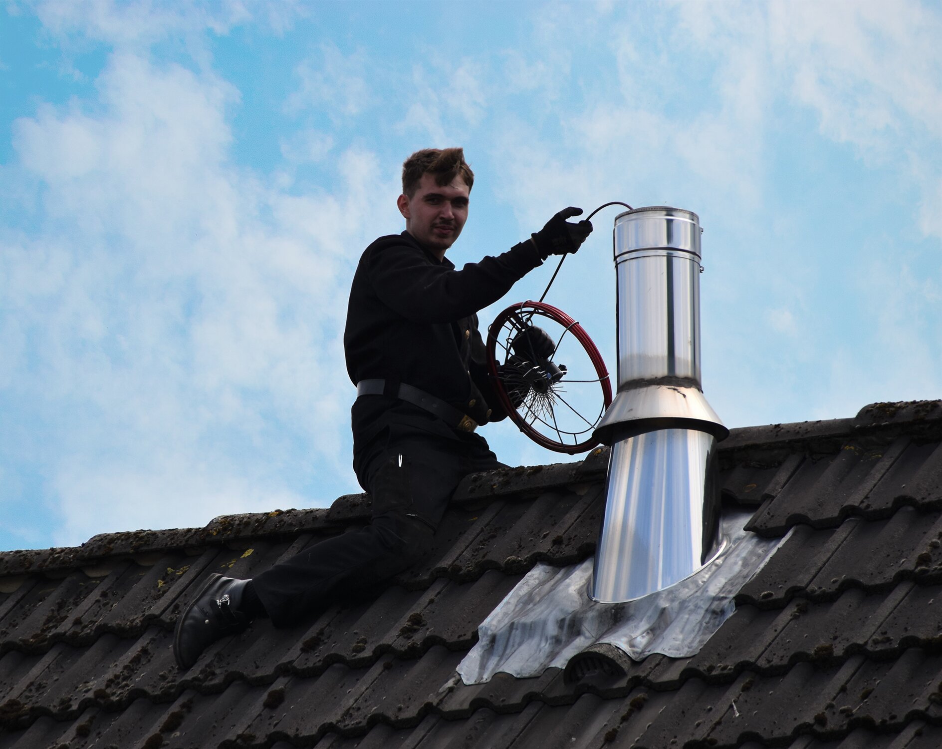 Schornsteinfeger auf einem Dach neben einem Edelstahlschornstein